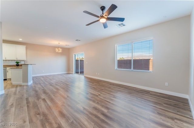 unfurnished living room featuring ceiling fan with notable chandelier and light wood-type flooring