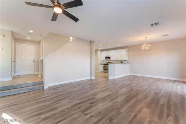 unfurnished living room featuring wood-type flooring and ceiling fan with notable chandelier