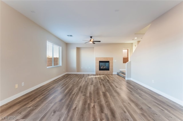 unfurnished living room with a tile fireplace, hardwood / wood-style floors, and ceiling fan