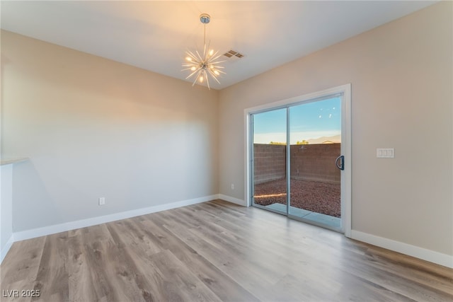 empty room with a notable chandelier and light hardwood / wood-style floors