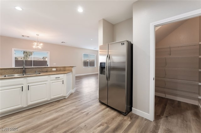 kitchen with sink, white cabinetry, hanging light fixtures, light hardwood / wood-style flooring, and stainless steel fridge