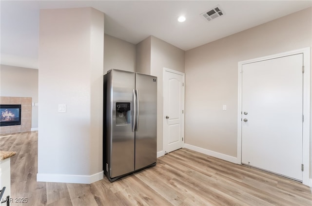 kitchen with a tiled fireplace, stainless steel fridge, and light hardwood / wood-style floors