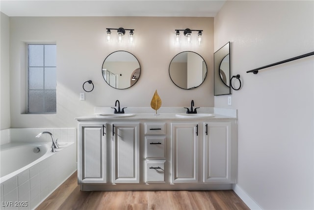 bathroom with hardwood / wood-style flooring, vanity, and tiled bath