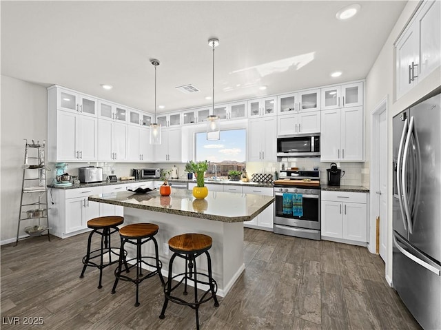 kitchen with white cabinetry, dark hardwood / wood-style floors, a kitchen island, pendant lighting, and stainless steel appliances