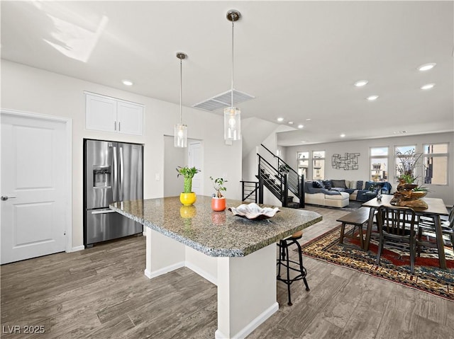 kitchen with pendant lighting, stainless steel fridge, white cabinetry, a kitchen breakfast bar, and stone countertops