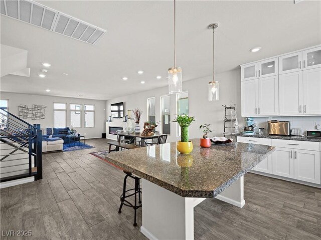 kitchen with a kitchen island, dark hardwood / wood-style floors, white cabinetry, a breakfast bar area, and dark stone counters