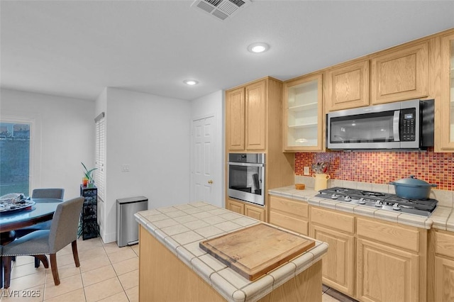 kitchen featuring stainless steel appliances, tile counters, light brown cabinetry, and recessed lighting