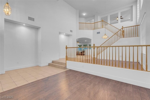 stairs with wood-type flooring, a towering ceiling, and ceiling fan with notable chandelier