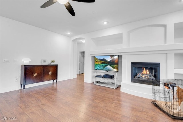 living room with a ceiling fan, recessed lighting, wood finished floors, a glass covered fireplace, and arched walkways
