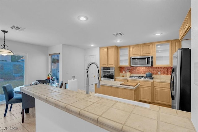 kitchen featuring appliances with stainless steel finishes, tile countertops, light brown cabinetry, hanging light fixtures, and light tile patterned floors