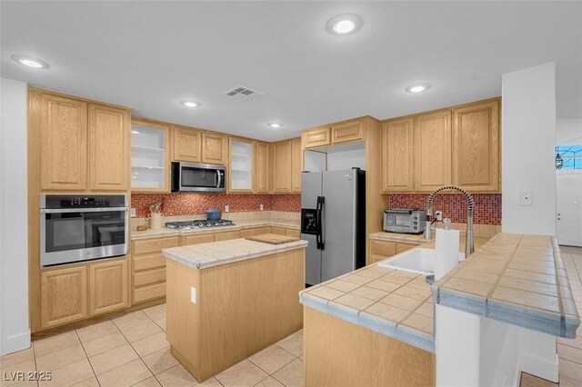 kitchen featuring light brown cabinetry, tile counters, stainless steel appliances, and a center island