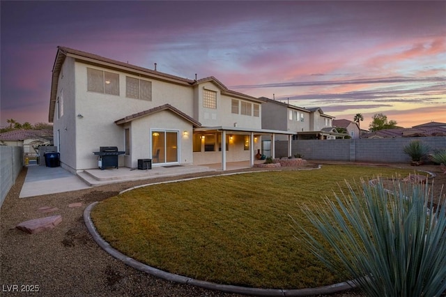 back house at dusk featuring a yard and a patio