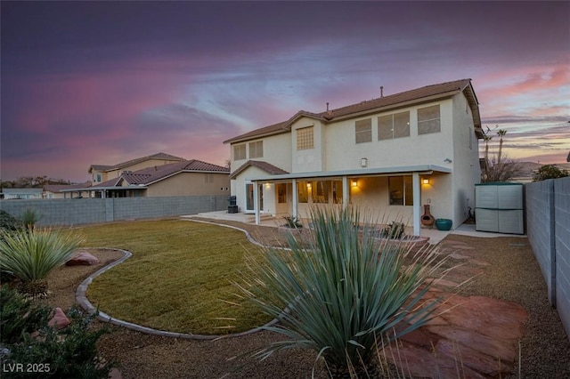 back house at dusk with a patio area and a lawn