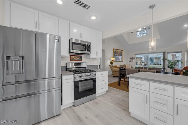 kitchen with appliances with stainless steel finishes, light hardwood / wood-style floors, white cabinets, decorative light fixtures, and vaulted ceiling