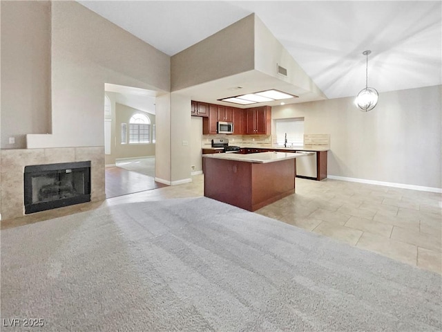 kitchen with a tiled fireplace, decorative light fixtures, vaulted ceiling, and stainless steel appliances