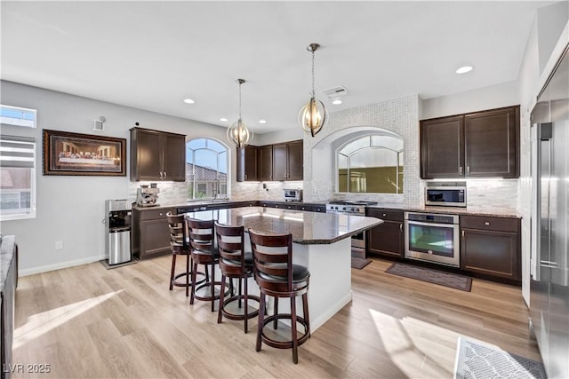 kitchen featuring appliances with stainless steel finishes, a breakfast bar, pendant lighting, a center island, and dark brown cabinets