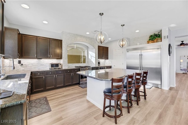 kitchen with dark brown cabinetry, sink, a center island, high quality appliances, and stone counters