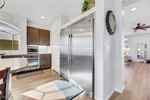 kitchen with light stone counters, dark brown cabinets, stainless steel appliances, light hardwood / wood-style floors, and backsplash