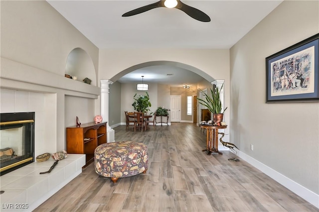 living area with ceiling fan, wood-type flooring, a tile fireplace, and built in features