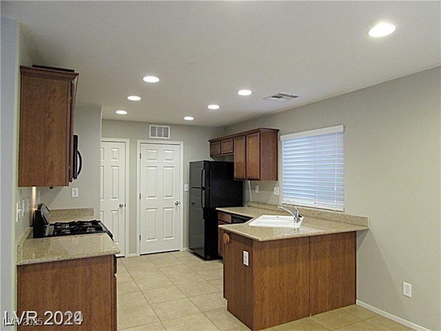 kitchen with light tile patterned flooring, black refrigerator, sink, range, and kitchen peninsula