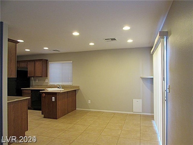 kitchen with black refrigerator, kitchen peninsula, sink, and light tile patterned floors