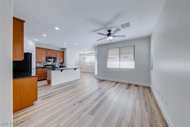 kitchen with backsplash, a kitchen breakfast bar, light hardwood / wood-style floors, and black appliances