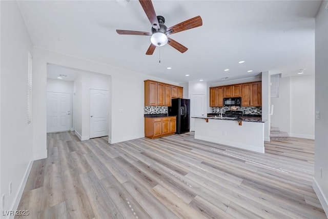 kitchen with a breakfast bar, decorative backsplash, black appliances, a center island with sink, and light hardwood / wood-style flooring