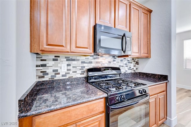 kitchen featuring dark stone countertops, decorative backsplash, light hardwood / wood-style floors, and black appliances