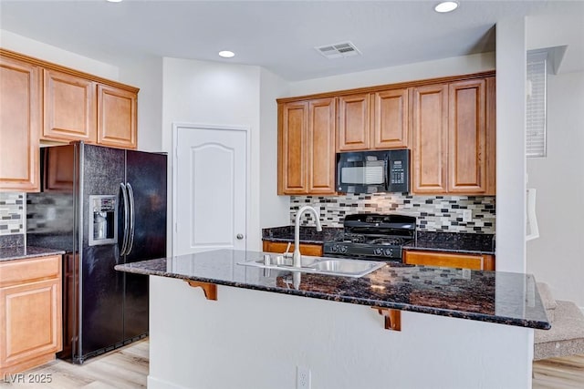 kitchen featuring sink, a breakfast bar area, a center island with sink, dark stone countertops, and black appliances