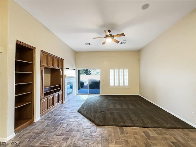 unfurnished living room with ceiling fan and built in shelves