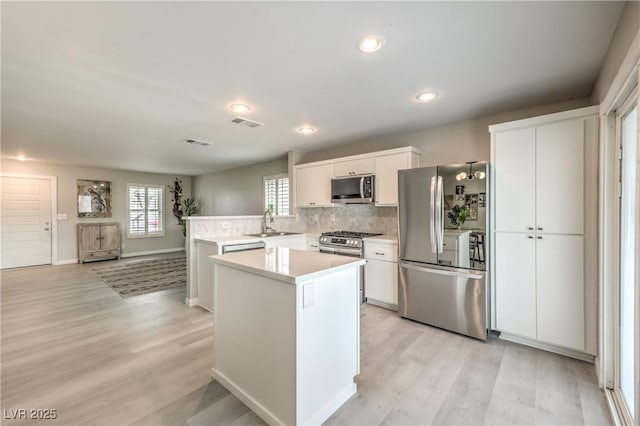 kitchen with white cabinetry, appliances with stainless steel finishes, kitchen peninsula, a kitchen island, and light hardwood / wood-style floors