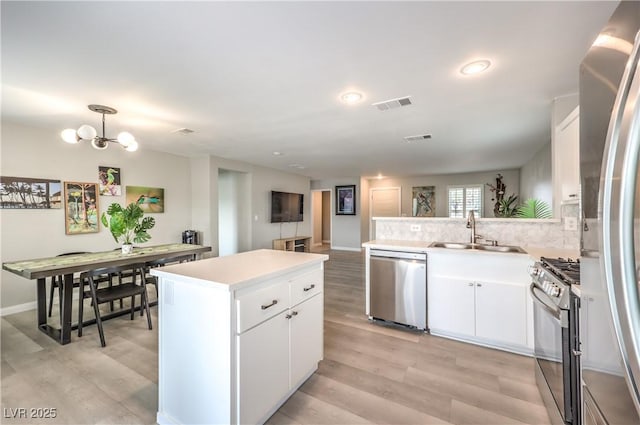 kitchen with sink, appliances with stainless steel finishes, white cabinetry, tasteful backsplash, and decorative light fixtures