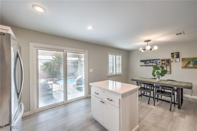 kitchen with stainless steel fridge, white cabinets, decorative light fixtures, a chandelier, and light wood-type flooring