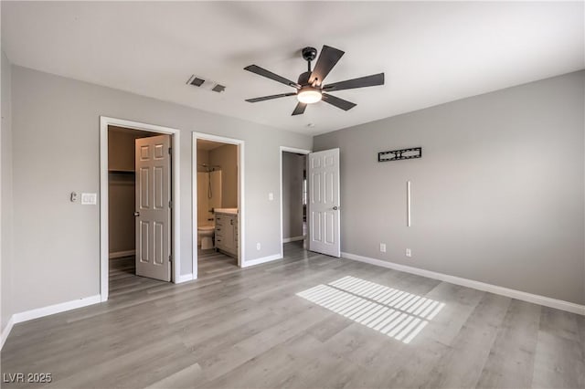 unfurnished bedroom featuring ensuite bath, ceiling fan, light hardwood / wood-style floors, a walk in closet, and a closet