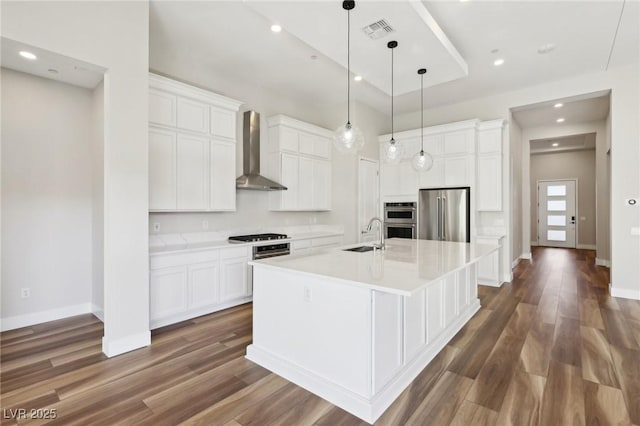 kitchen with appliances with stainless steel finishes, wall chimney exhaust hood, a center island with sink, and white cabinets