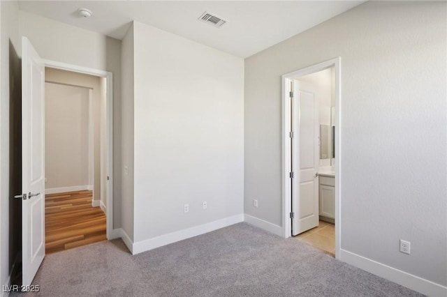 unfurnished bedroom featuring light colored carpet and connected bathroom