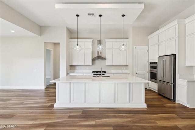 kitchen featuring wall chimney exhaust hood, sink, white cabinetry, appliances with stainless steel finishes, and a kitchen island with sink