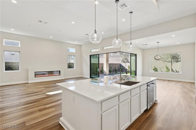 kitchen featuring a kitchen island with sink, sink, white cabinetry, and decorative light fixtures