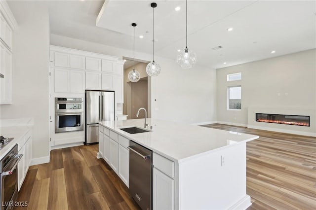 kitchen featuring sink, white cabinetry, stainless steel appliances, a center island with sink, and decorative light fixtures