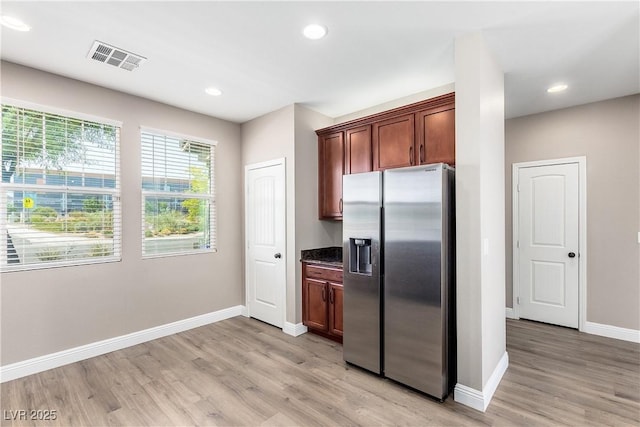 kitchen featuring dark stone counters, stainless steel fridge with ice dispenser, and light wood-type flooring