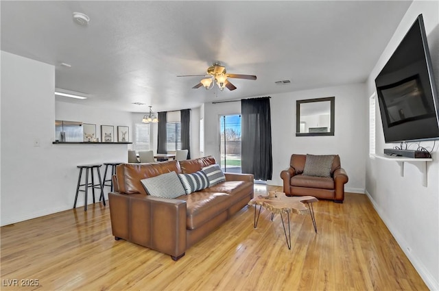 living room featuring ceiling fan with notable chandelier and light hardwood / wood-style flooring