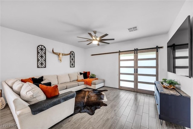 living room featuring ceiling fan, wood-type flooring, and a barn door