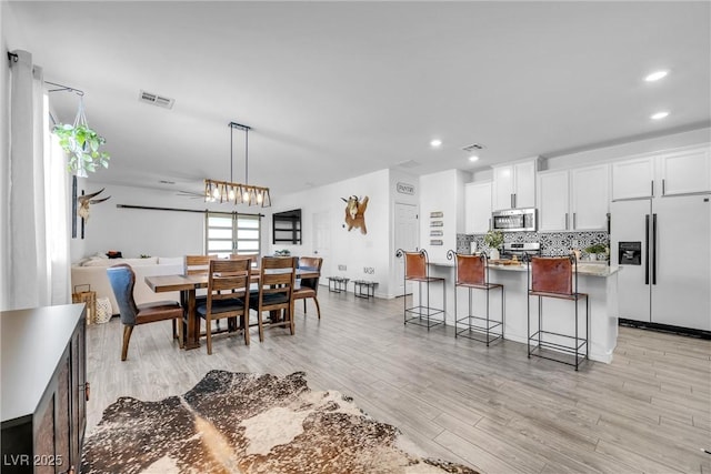 kitchen with white cabinetry, refrigerator with ice dispenser, pendant lighting, and a breakfast bar area