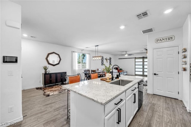 kitchen featuring sink, a breakfast bar area, light hardwood / wood-style flooring, a kitchen island with sink, and white cabinets