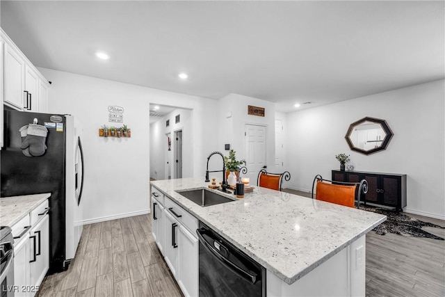 kitchen featuring an island with sink, black dishwasher, sink, white cabinets, and light stone countertops