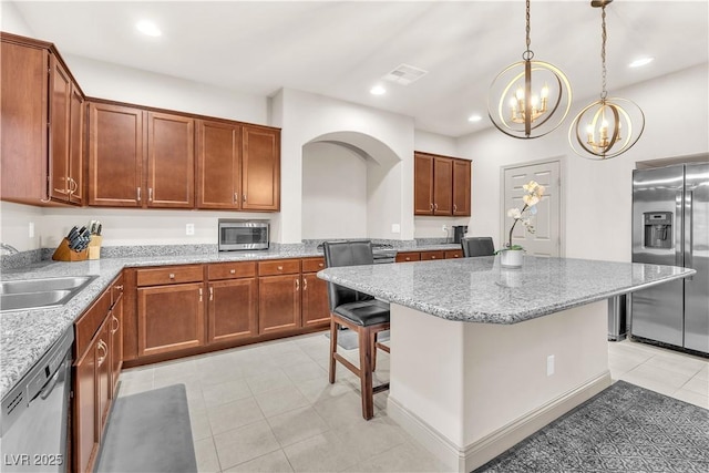 kitchen featuring light tile patterned floors, a kitchen bar, stainless steel appliances, a kitchen island, and decorative light fixtures