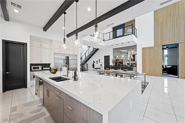 kitchen with pendant lighting, sink, white cabinetry, and a large island with sink