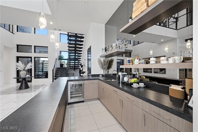 kitchen with light tile patterned flooring, sink, pendant lighting, a towering ceiling, and beverage cooler