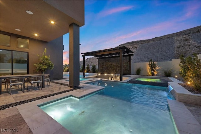 pool at dusk featuring a patio area, pool water feature, and an in ground hot tub