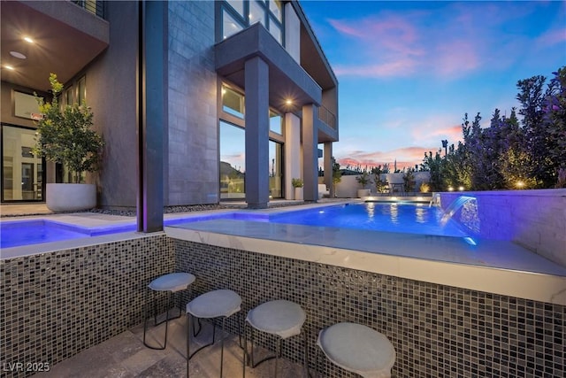 pool at dusk featuring pool water feature and a jacuzzi